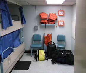 Matt's berth, which is a small room with bunked single-person beds, two chairs, two life jackets and immersion suits, and access to a shared bathroom. The room is about 12 feet long and 10 feet wide.